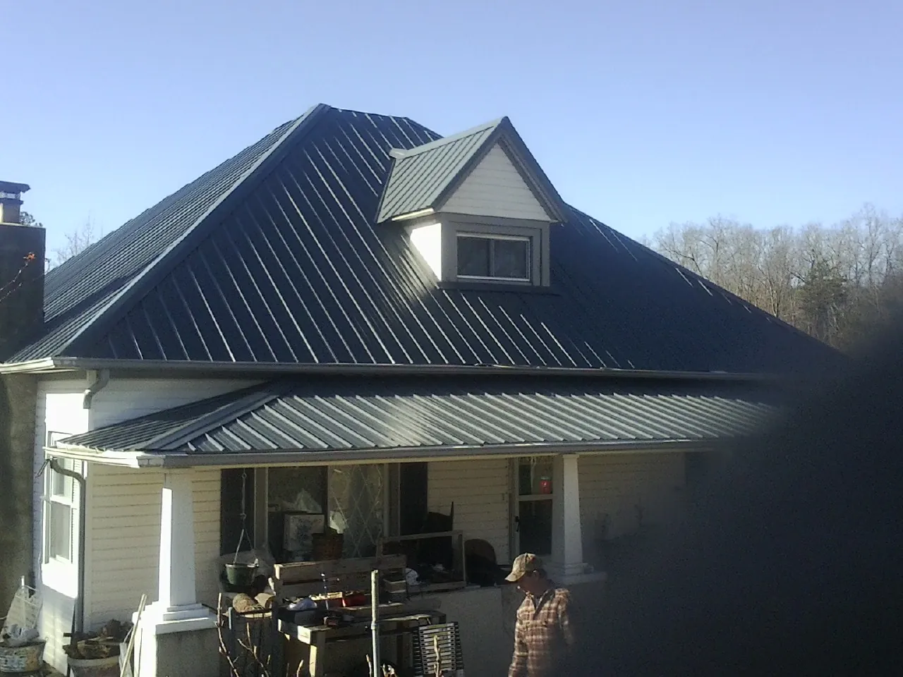 Dark blue standing seam metal roof with a dormer above a front porch in Hayden