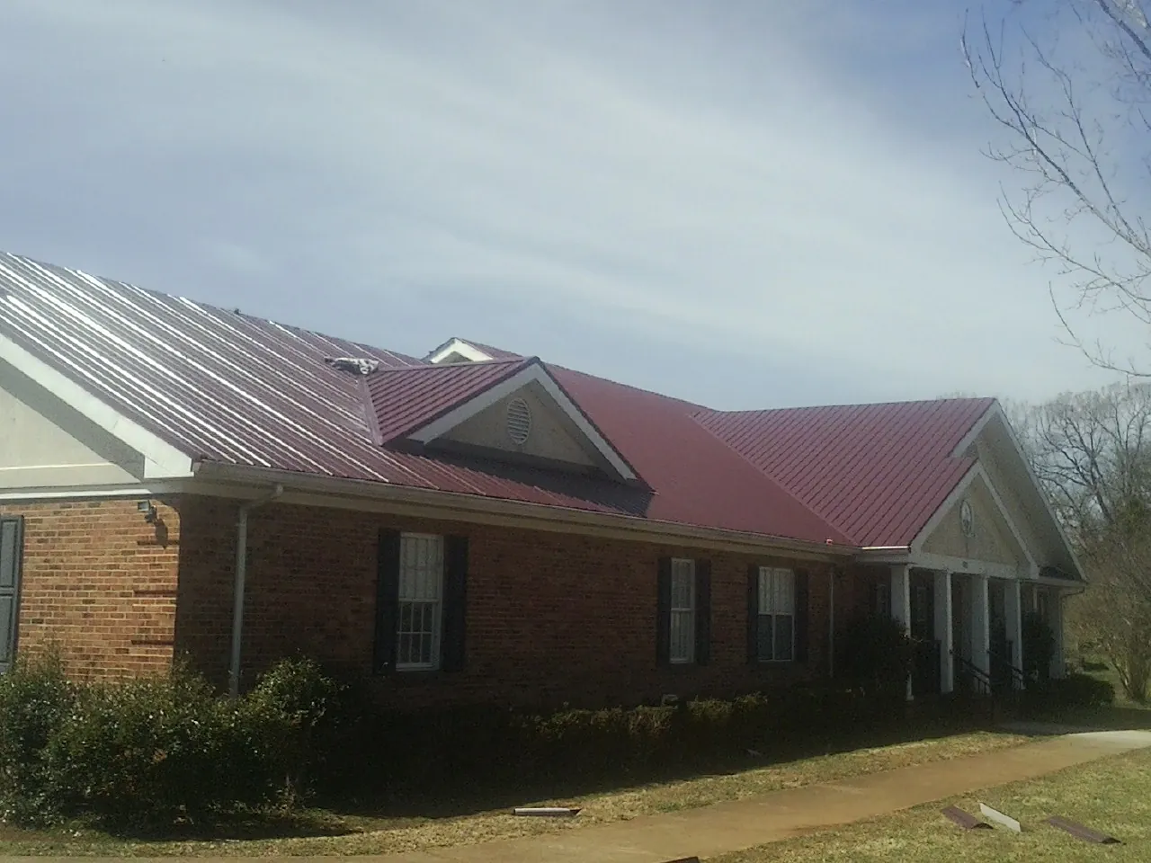 Red metal roof with gabled entries on a long brick building, from a Hail Damage Roof Repair job in Hayden