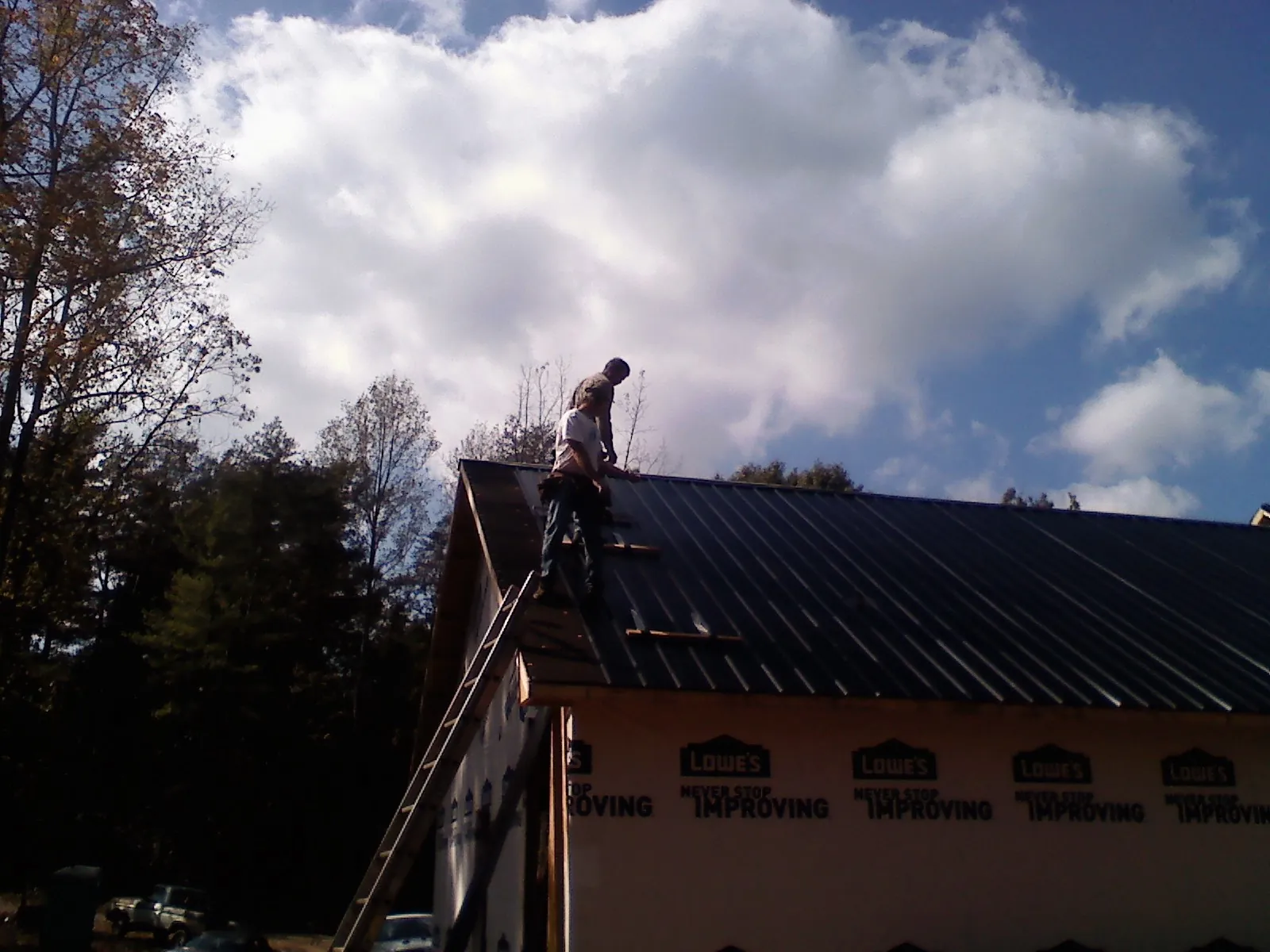 Roofer fastening dark metal panels high against a cloudy sky, from a Roof Inspection job in Hayden