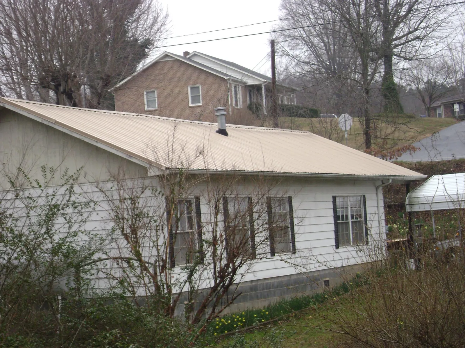 Tan metal roof on a white sided house set into a hillside — Commercial Roofing by Roofing Brothers in Hayden